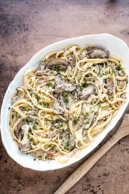 A serving dish of duck confit pasta made with duck confit legs, mushrooms garlic, shallots, fettuccine, garlic, cream, wine, and Parmesan cheese.