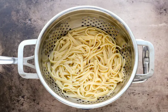 Fettuccine draining in a stainless steel colander.