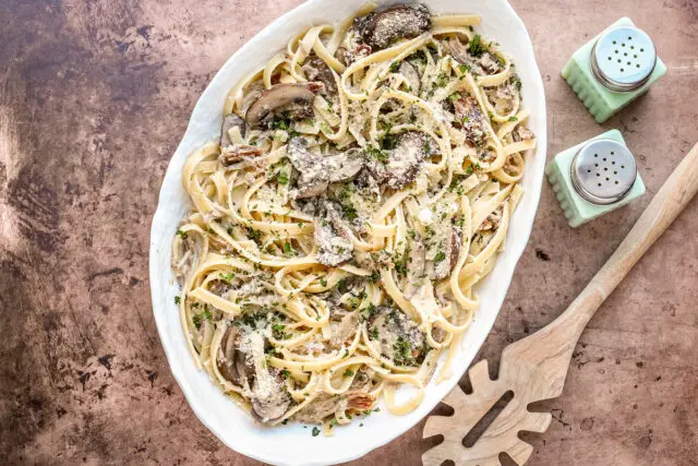 A serving dish of duck confit pasta made with duck confit legs, mushrooms garlic, shallots, fettuccine, garlic, cream, wine, and Parmesan cheese.