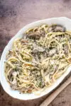 A serving dish of duck confit pasta made with duck confit legs, mushrooms garlic, shallots, fettuccine, garlic, cream, wine, and Parmesan cheese.