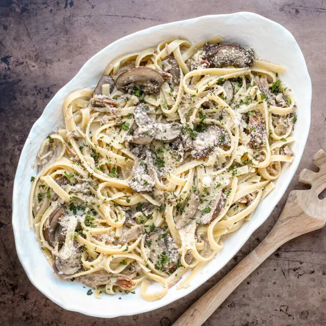 A serving dish of duck confit pasta made with duck confit legs, mushrooms garlic, shallots, fettuccine, garlic, cream, wine, and Parmesan cheese.