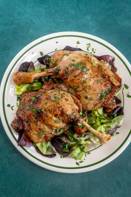 Duck confit with parsley garnish on a plate.