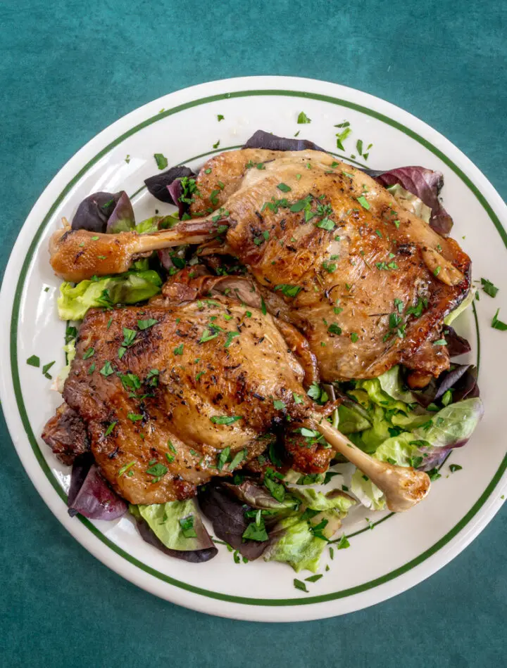 Duck confit with parsley garnish on a plate.