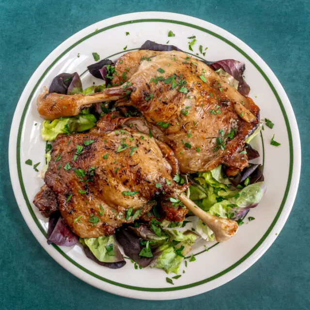 Duck confit with parsley garnish on a plate.