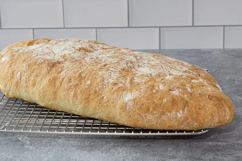 A loaf of ciabatta bread on a cooling rack.