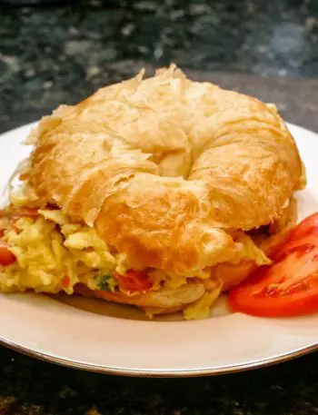 egg croissant sandwich with scrambled eggs, ham, and tomato