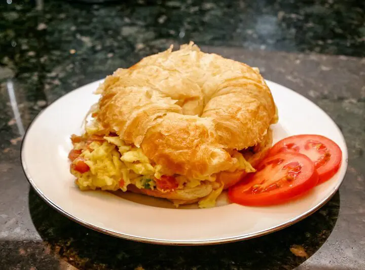 egg croissant sandwich with scrambled eggs, ham, and tomato