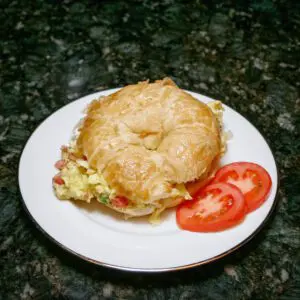 scrambled egg croissant sandwich on a plate with tomatoes