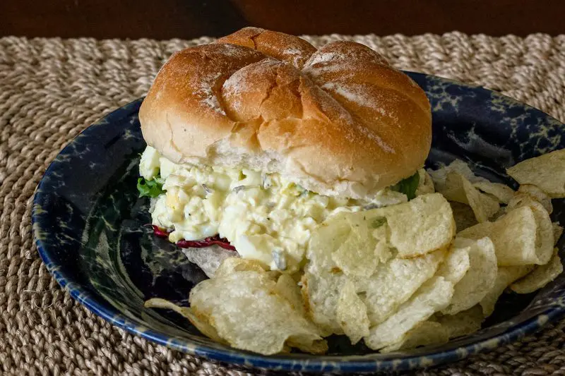egg salad sandwich filling on a bun with lettuce and chips