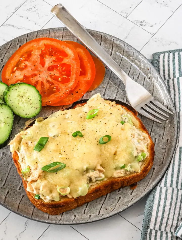 A tuna melt serving with sliced tomatoes and cucumbers on the side.