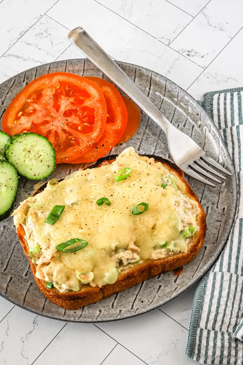 A tuna melt serving with sliced tomatoes and cucumbers on the side.