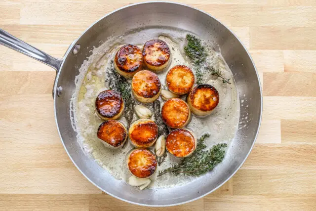 Butter, smashed garlic, and thyme are added to the skillet to flavor the fondant potatoes.