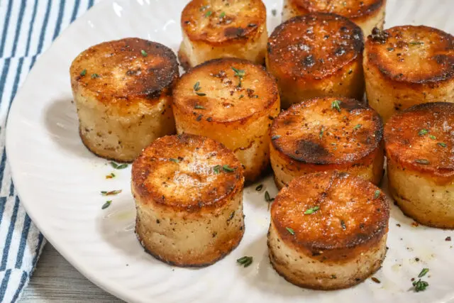 Closeup of fondant potatoes on a plate with thyme leaves for garnish.