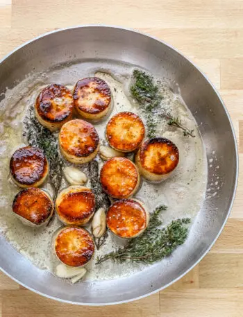 Butter, smashed garlic, and thyme are added to the skillet to flavor the fondant potatoes.