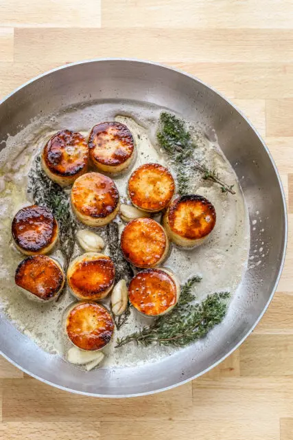 Butter, smashed garlic, and thyme are added to the skillet to flavor the fondant potatoes.