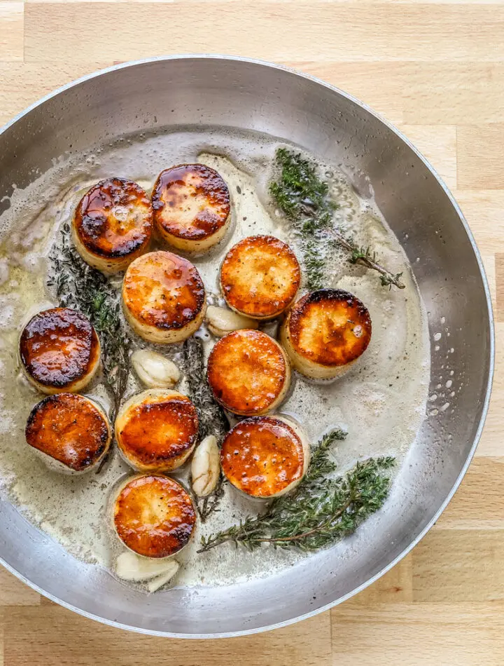 Butter, smashed garlic, and thyme are added to the skillet to flavor the fondant potatoes.