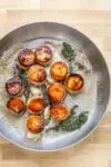 Butter, smashed garlic, and thyme are added to the skillet to flavor the fondant potatoes.