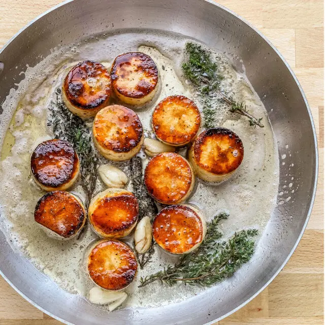 Butter, smashed garlic, and thyme are added to the skillet to flavor the fondant potatoes.