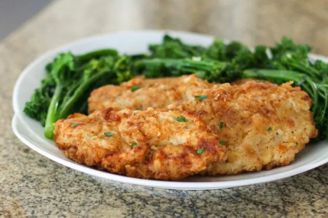 fried chicken breast cutlets on a plate with broccolini