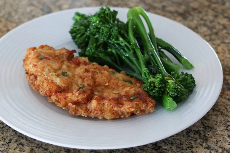 Fried chicken breasts on a plate with broccolini on the side.
