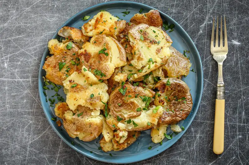 crispy fried smashed potatoes on a plate with parsley garnish