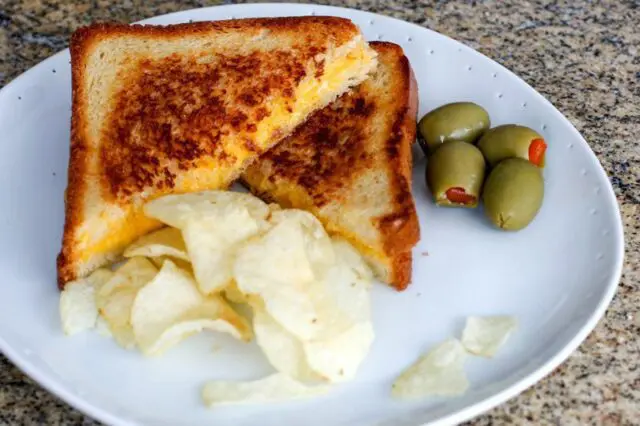 grilled cheese sandwich with chips and olives on the side.