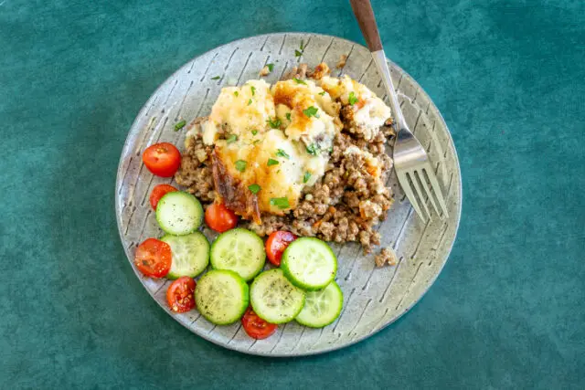 Ground beef casserole with cheesy mashed potato topping and some cucumbers and tomatoes on the side.