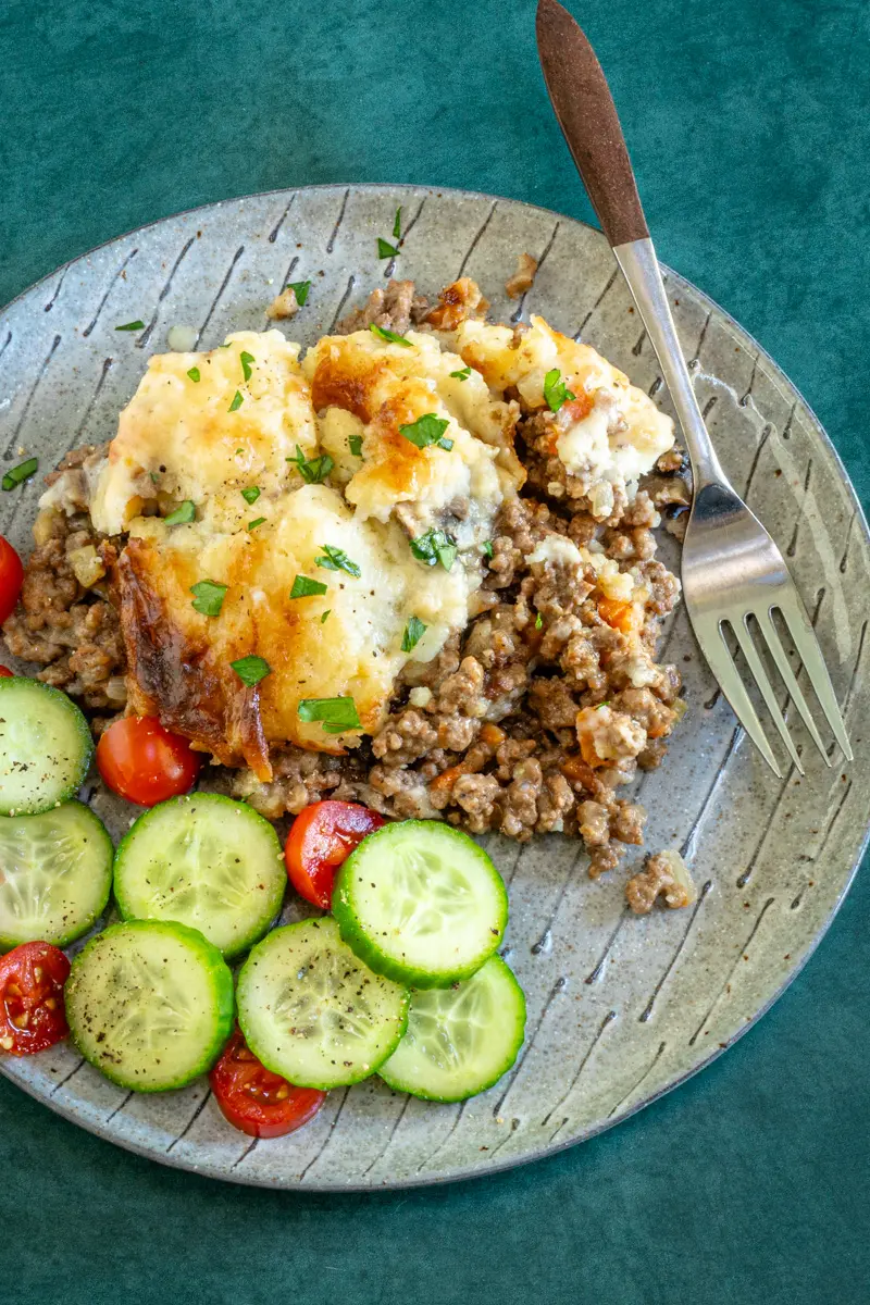 Ground beef casserole with cheesy mashed potato topping and some cucumbers and tomatoes on the side.