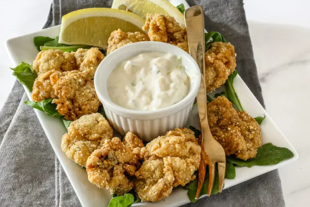 A ramekin with homemade tartar sauce shown with fried oysters.