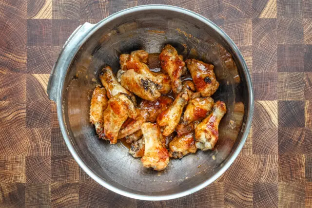 Tossing hot honey chicken wings with the hot sauce, butter, and lime zest.