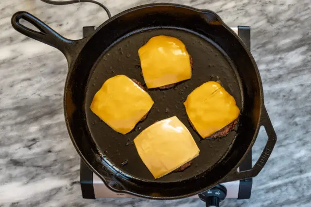 Add cheese to the burgers in the pan and continue cooking until it has melted.