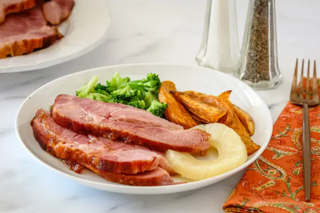 Instant Pot baked ham sliced and served with sweet potato fries, pineapple, and broccoli.