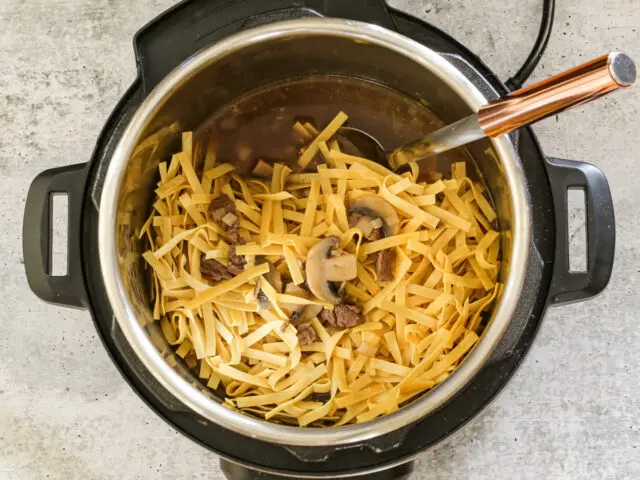 Adding the noodles to the stroganoff in the Instant Pot.