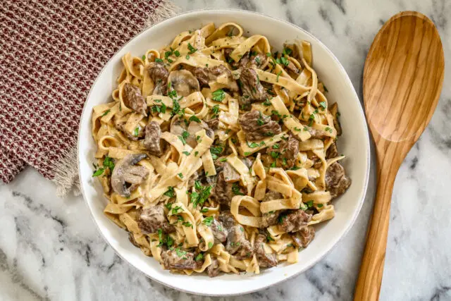 A serving bowl with Instant Pot stroganoff made with top sirloin beef, noodles, mushrooms, and sour cream.