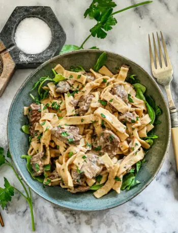 A bowl of Instant Pot beef stroganoff with parsley and arugula.