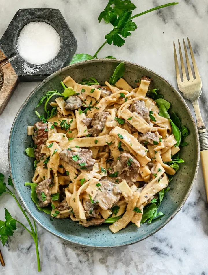 A bowl of Instant Pot beef stroganoff with parsley and arugula.