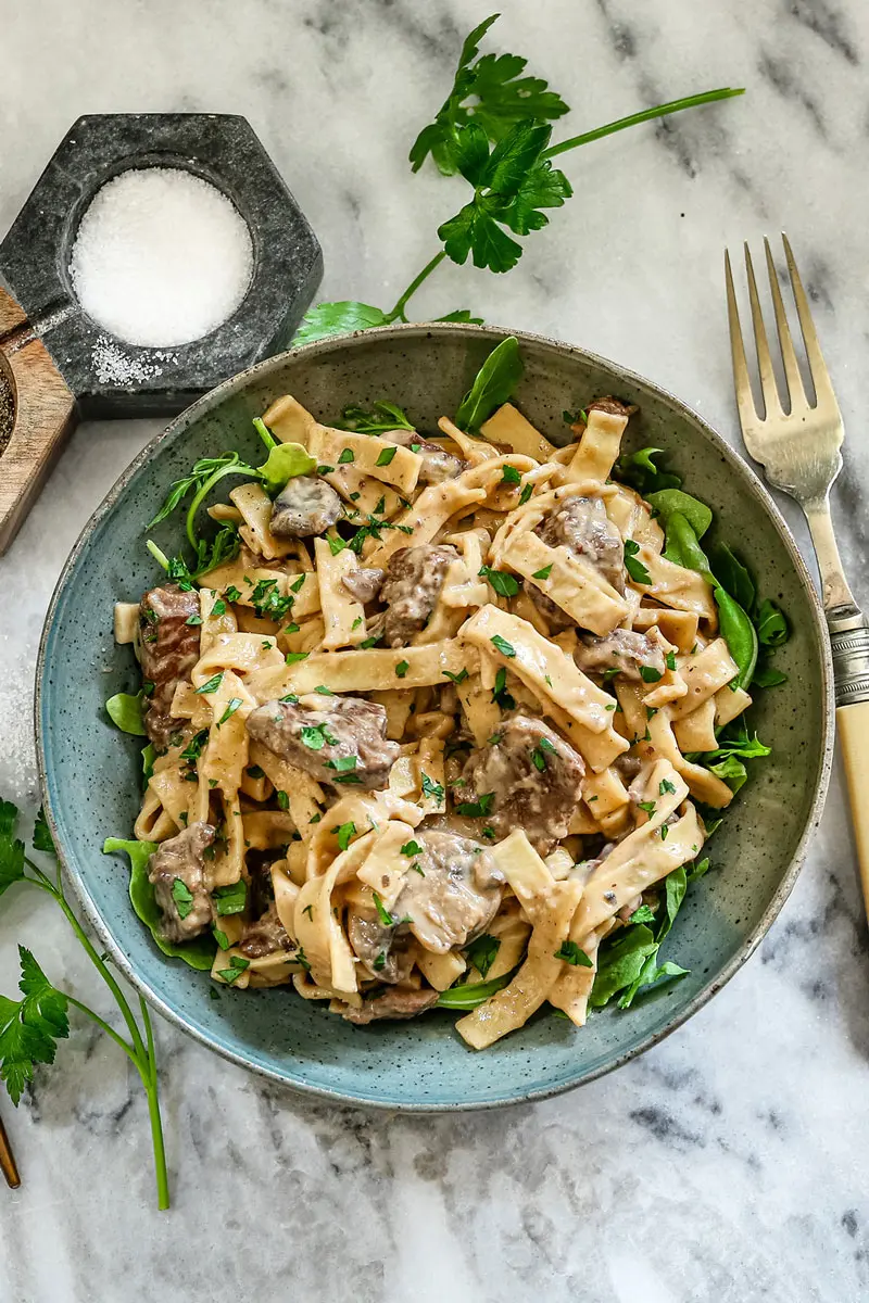 A bowl of Instant Pot beef stroganoff with parsley and arugula.