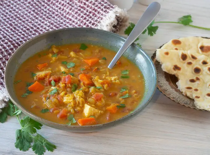 a bowl of mulligatawny soup with naan bread on the side