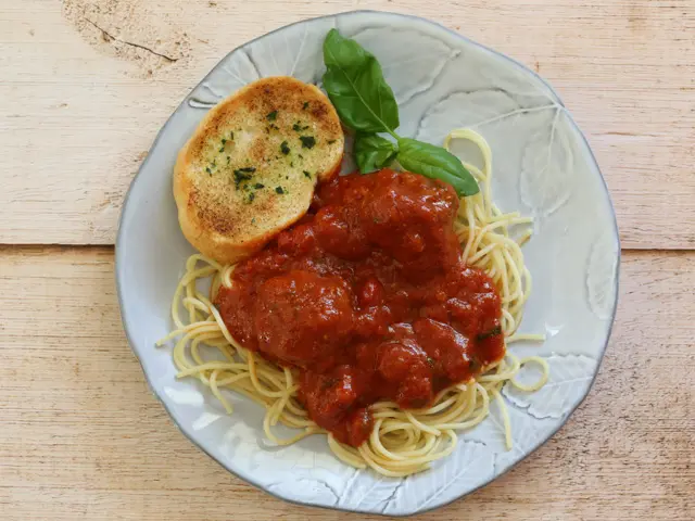 Meatballs and sauce shown on spaghetti with garlic bread.