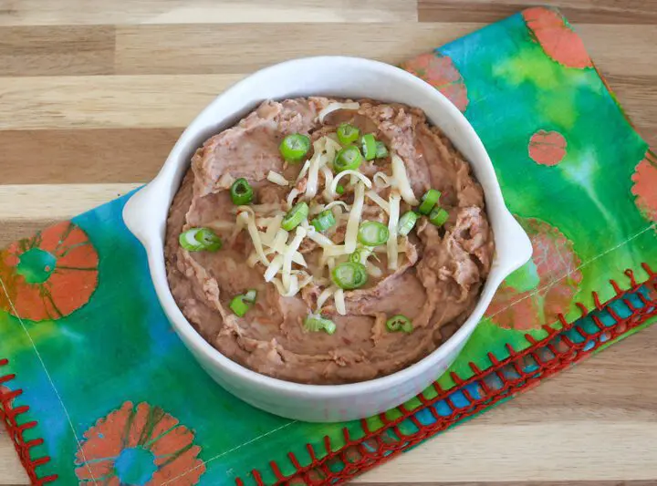 instant pot refried beans in a bowl with cheese and green onion garnish