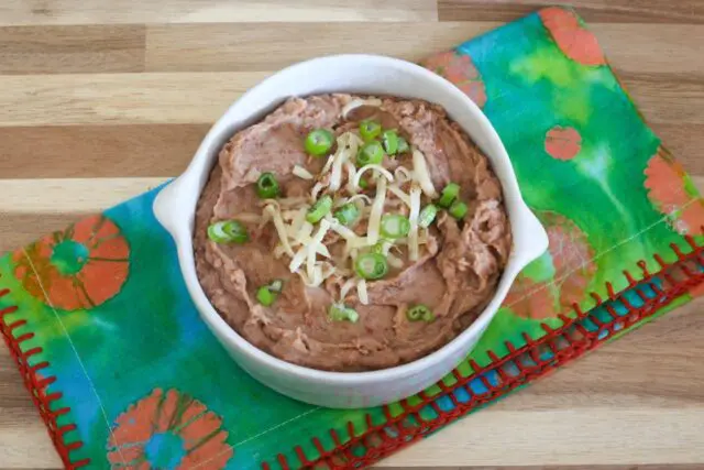 instant pot refried beans in a bowl with cheese and green onion garnish