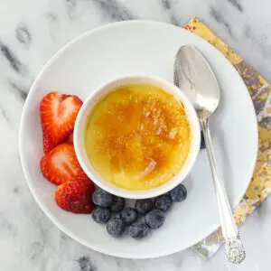 A ramekin of crème brulée with berries on the side