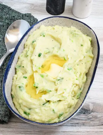 A serving bowl with Irish champ mashed potatoes and scallions with butter melting on top.