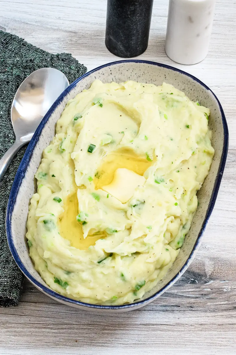 A serving bowl with Irish champ mashed potatoes and scallions with butter melting on top.