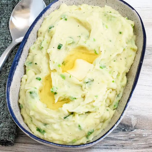 A serving bowl with Irish champ mashed potatoes and scallions with butter melting on top.