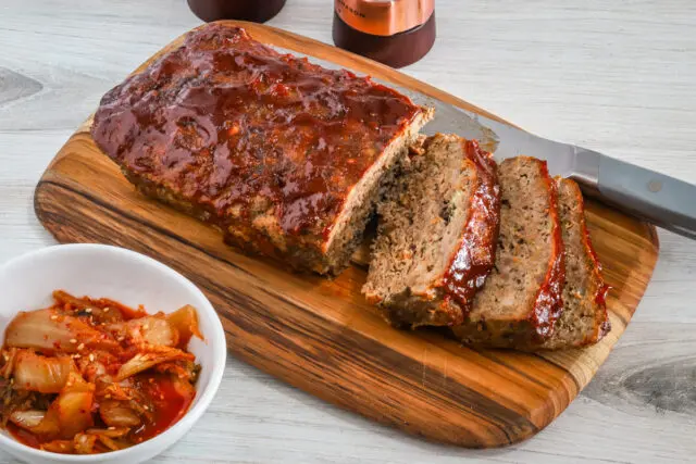 Korean meatloaf on a cutting board, sliced with kimchi on the side.