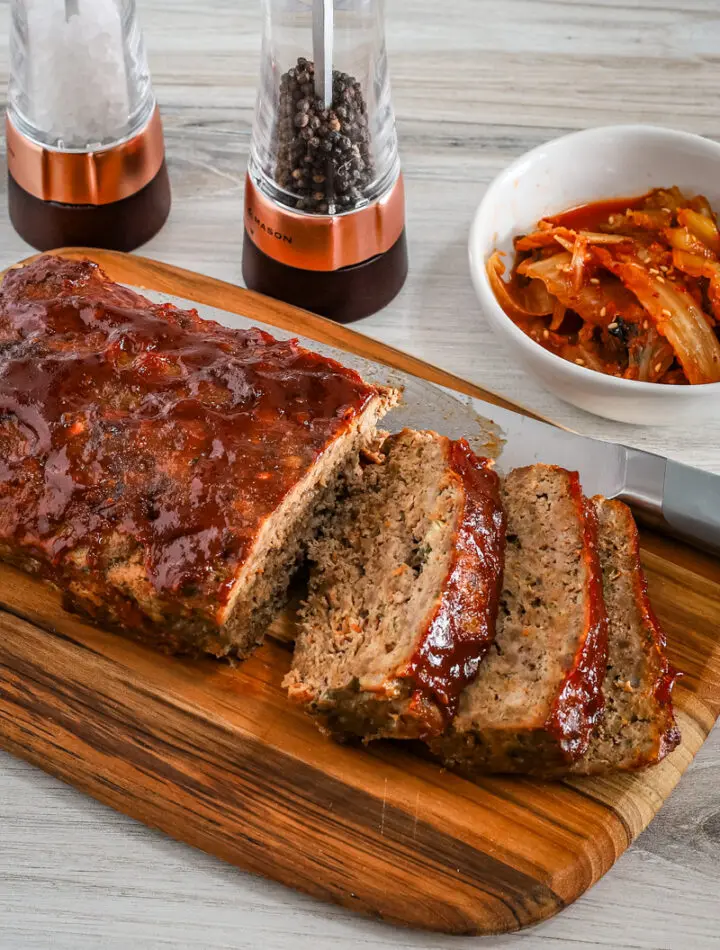 Korean meatloaf on a cutting board, sliced with kimchi on the side.