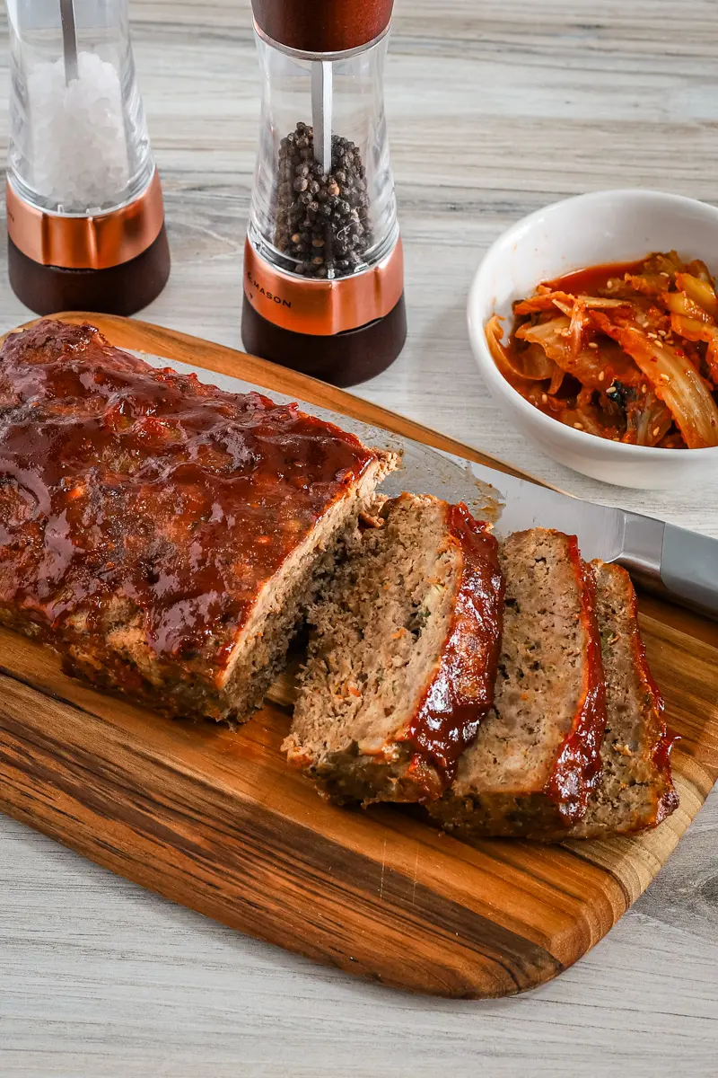 Korean meatloaf on a cutting board, sliced with kimchi on the side.