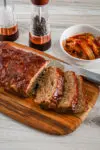 Korean meatloaf on a cutting board, sliced with kimchi on the side.