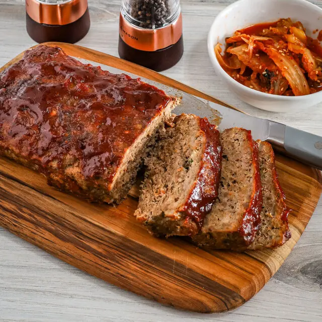 Korean meatloaf on a cutting board, sliced with kimchi on the side.